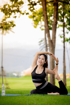 Young Asian woman practicing yoga outdoors in green park at sunrise