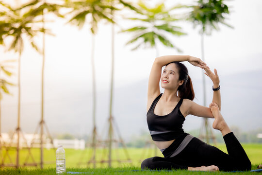 Young Asian woman practicing yoga outdoors in green park at sunrise