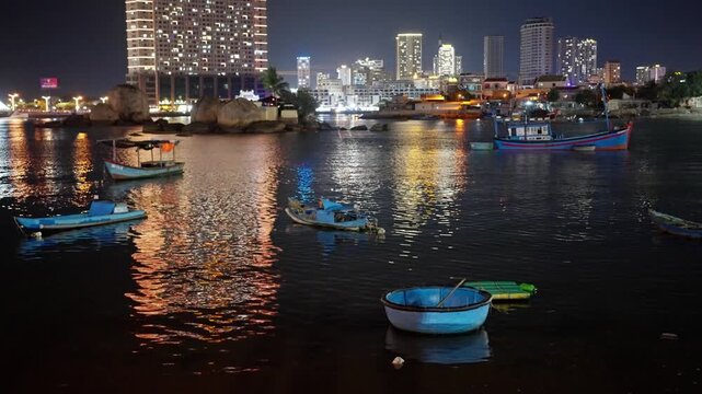 Nha Trang Vietnam. 01 06 2026 Night harbor panorama with coracle and fishing boats against illuminated city skyline with colorful water reflections and gentle