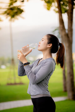 Young Asian woman drinking water after outdoor workout in the park
