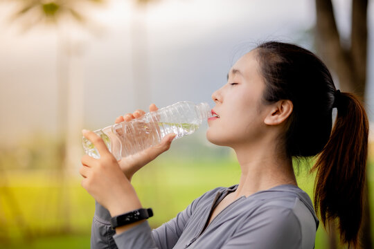 Young Asian woman drinking water after outdoor workout in the park
