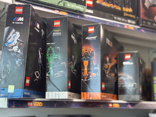 Fototapeta premium Rows of lego model boxes displayed on a store shelf in a toy aisle, with racing and space sets visible in a blurred retail background.