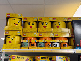 Fototapeta premium Toy store shelf with stacked lego boxes and halloween-themed storage heads in bright yellow colors on a retail display