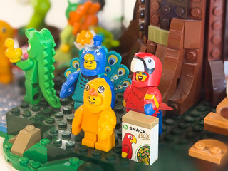 Obraz premium Colorful toy animals and bird figures in a jungle play scene with a snack box, showing a playful and creative building set on a green base.