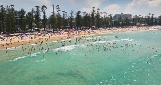 Manly Beach in Sydney, Australia, bustling with numerous people enjoying a sunny summer day, swimming in the turquoise ocean water and relaxing on the sandy shore. Summer vacation, travel, relax