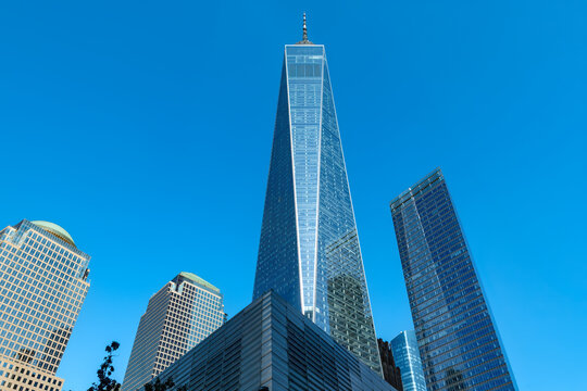 Low angle view looking up at the iconic One World Trade Center tower surrounded by modern corporate skyscrapers in downtown Manhattan, New York.