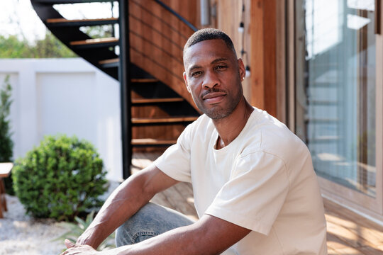 Man sits outside modern home with spiral staircase.