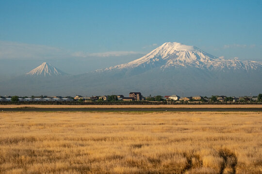 YEREVAN, ARMENIA - JUNE 7, 2026: Scenic panoramic view of the majestic snow-capped Mount Ararat and Little Ararat rising above rural houses, captured from Zvartnots International Airport.