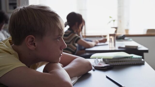 Caucasian teenage boy resting head on desk in classroom, waking up and looking tiredly towards front. Clip for educational campaigns on student fatigue