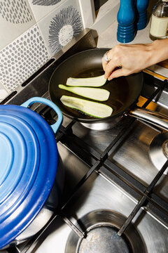 hand cooking zucchini in frying pan for healthy home dinner with flash