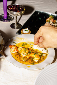 Hand dipping bread into prawn sauce at shared dinner table