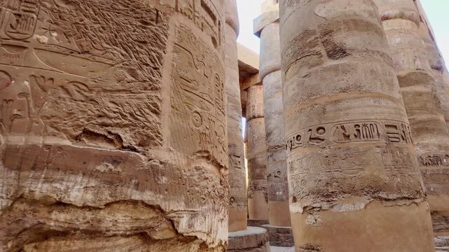 First-person view walking through Majestic columns with ancient egyptian hieroglyphic carvings inside the great hypostyle hall of the karnak temple complex in luxor, egypt
