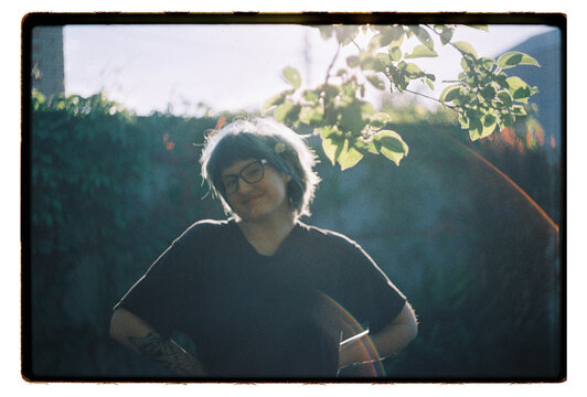 A woman smiles softly in a sun-drenched backyard garden