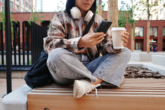 Student with phone and coffee sitting on campus bench