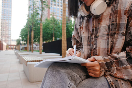 Student writing in notebook with headphones at university campus