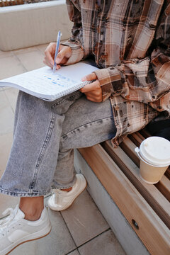 Student writing notes in spiral notebook on campus bench