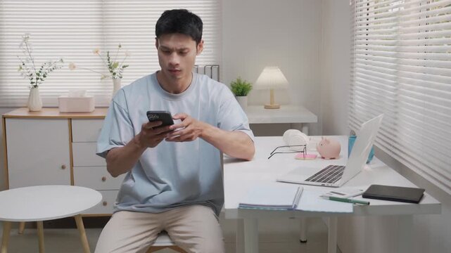 An Asian man, looking stressed about household finances, slumps down in his living room, showing signs of worry.