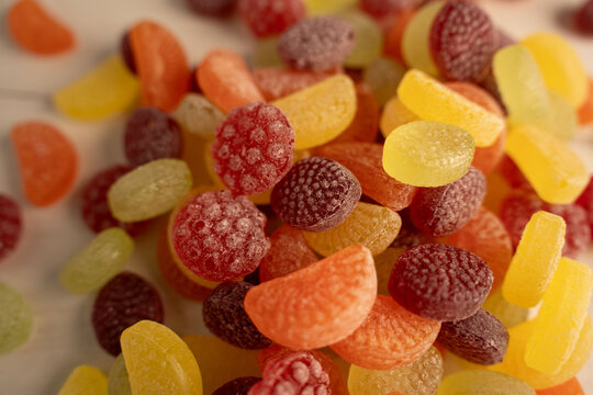 close-up of assorted colorful sugar-coated fruit gumdrops and citrus-shaped jelly candies scattered on a tabletop, warm soft light highlighting frosted textures and vibrant orange, yellow, red hues