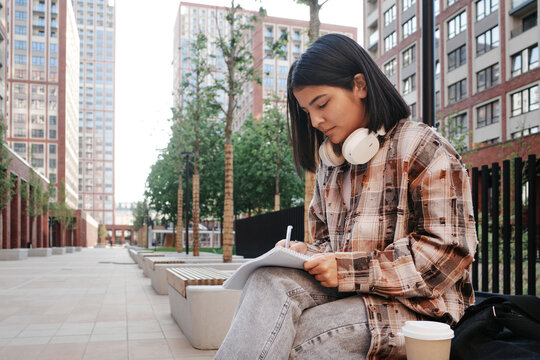 Student writing in notebook while sitting outdoors on campus