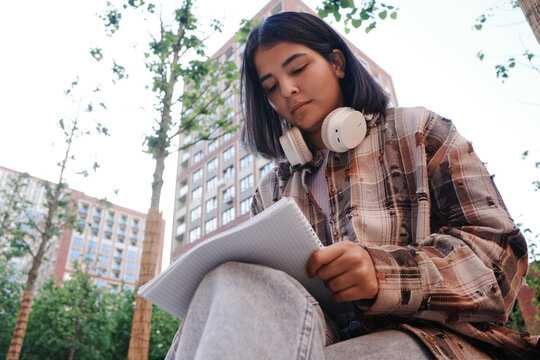 Student reading outdoors on university campus with headphones
