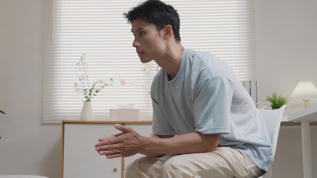 An Asian man, looking stressed about household finances, slumps down in his living room, showing signs of worry.