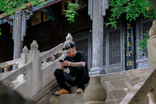 Asian Man Using Mobile Phone Sitting on Chinese Temple Stone Stairs.