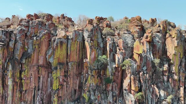 Cinematic aerial footage of a massive red sandstone escarpment towering over the dry, flat savanna plains in Namibia, Africa. Epic geological landscape.