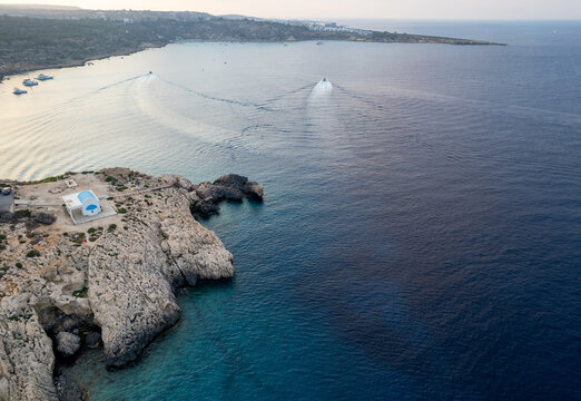 Drone aerial of Cape Greco peninsula with Agioi Anargyroi christian church on the rocks. Turquoise ocean water