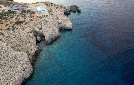 Drone aerial of Cape Greco peninsula with Agioi Anargyroi christian church on the rocks. Turquoise ocean water