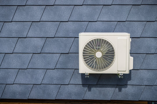 Outdoor air conditioning split unit mounted on a dark gray diamond-shaped shingle wall