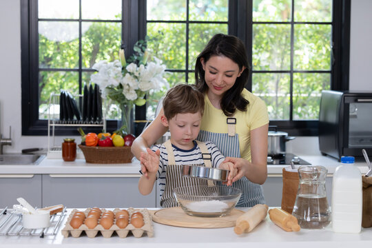 Mother helps her young son mix flour in a bowl on the kitchen counter
