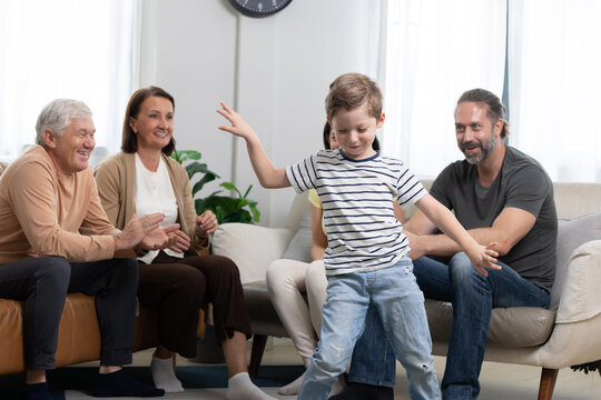 Child performs dance in living room while family watches and claps during gathering in afternoon