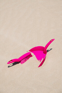 a pink dustpan and brush emerge from the sand