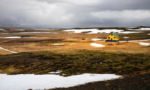 Charming isolated yellow house with a green roof in a desolate Icelandic tundra landscape under dark stormy skies.