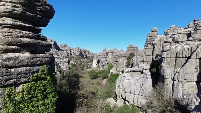 Drone aerial shot capturing massive layered limestone rock formations with green vegetation at El Torcal Alto, Spain, under clear blue sky.