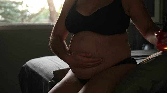 Expectant mother moisturizing her tummy with oil to prevent stretch marks