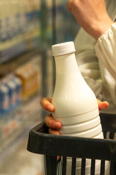 Close-Up of a Hand Holding a Bottle of Milk in a Grocery Basket Surrounded by Dairy Products