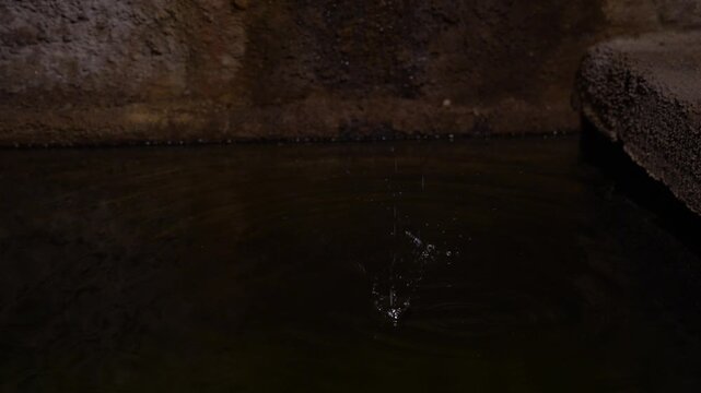 A water drop falls in slow motion into an old medieval stone cistern