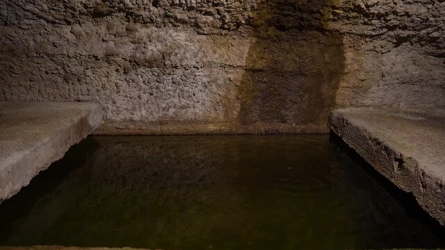 A water drop falls in slow motion into an old medieval stone cistern