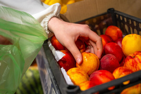 Selecting Fresh Fruits: A Hand Reaches for Juicy Peaches Among Vibrant Produce in a Market Setting