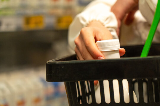 A Hand Holding a Bottle Inside a Shopping Basket at a Store, Highlighting the Act of Selecting Health Products in a Grocery Environment