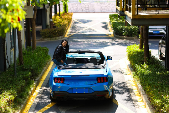 A stylish Asian girl stands on a blue convertible.