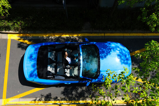 A stylish Asian girl sleeps inside a blue convertible.