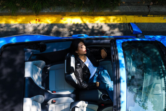 A stylish Asian girl sleeps inside a blue convertible.