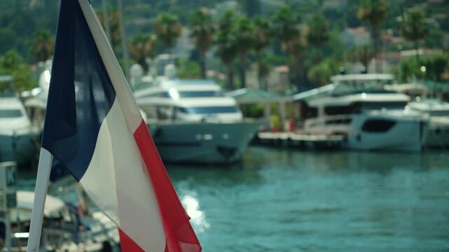 French tricolor flag waving in the wind with luxury yachts docked in a mediterranean harbor, representing travel and patriotism