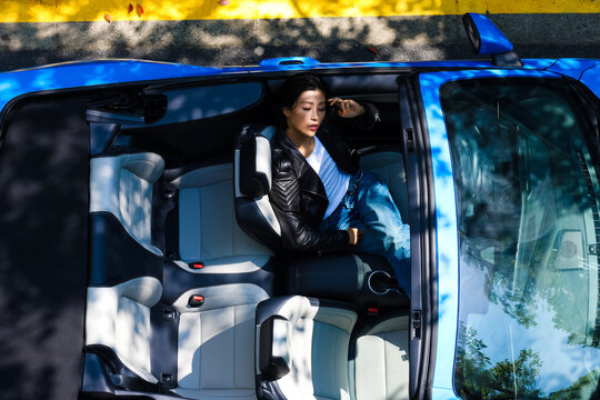 A stylish Asian girl sleeps inside a blue convertible.