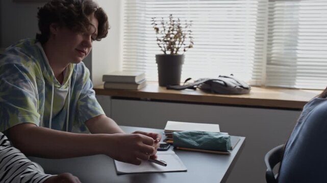 Caucasian teenage boy passing secret sticky note to classmate during high school lesson. Video for educational marketing, youth lifestyle ads, and school-themed commercial projects