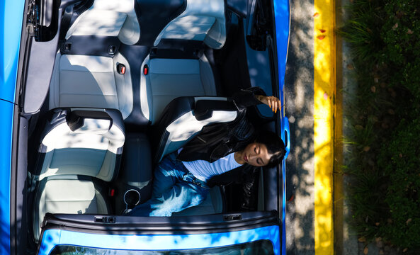 A stylish Asian girl sleeps inside a blue convertible.