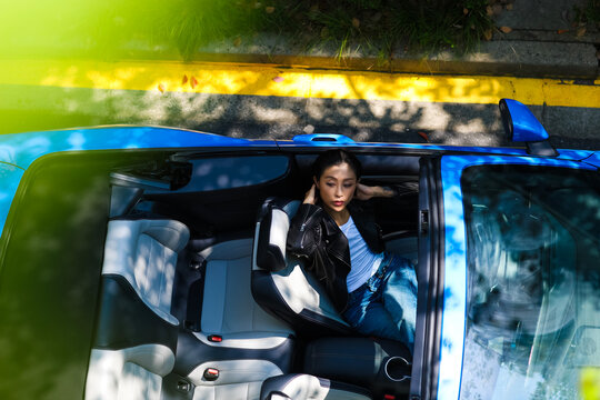 A stylish Asian girl sleeps inside a blue convertible.
