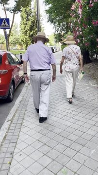 Paseo de dos se&ntilde;ores mayores con sombrero paseando viejos andando por acera calle tercera edad activo